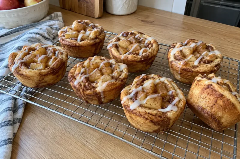 Cinnamon Roll Apple Pie Cups – golden cinnamon roll cups filled with apple pie filling and drizzled with icing on a cooling rack
