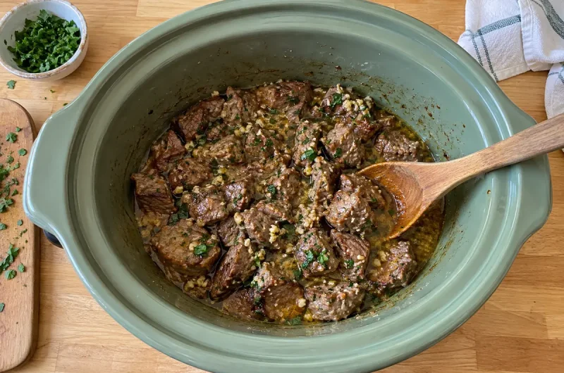 Crockpot Steak Bites – tender garlic butter steak bites with parsley in a sage green slow cooker crock
